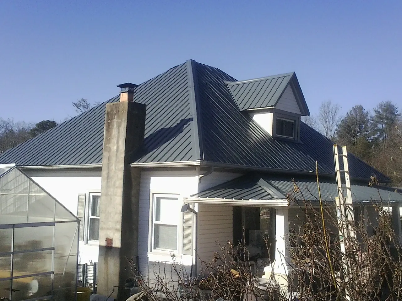 Dark blue standing seam metal roof on a white farmhouse with dormer — Slate & Tile Roof Repair by Roofing Brothers in Enigma