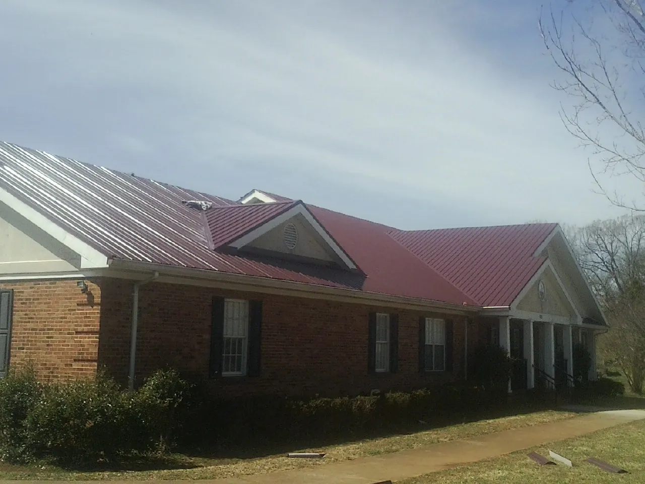 Red metal roof with gabled entries on a long brick building, from a Hail Damage Roof Repair job in Enigma