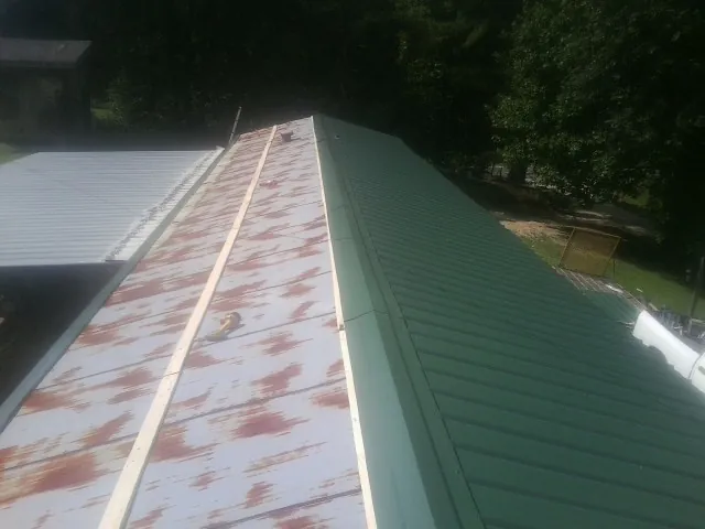 Old rusted panels beside newly installed green metal roofing — Wind Damage Roof Repair by Roofing Brothers in Enigma