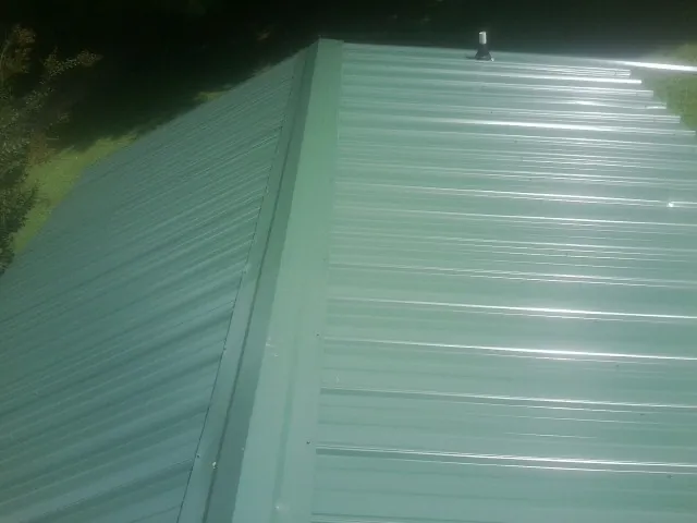 New green metal panels meeting at the ridge of a roof — Flat Roof Repair work by our crew in Enigma