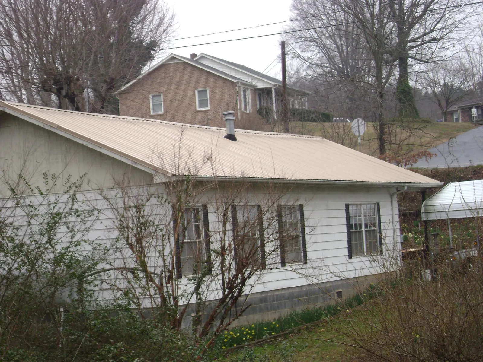 Tan metal roof on a white sided house set into a hillside — Commercial Roofing by Roofing Brothers in Enigma