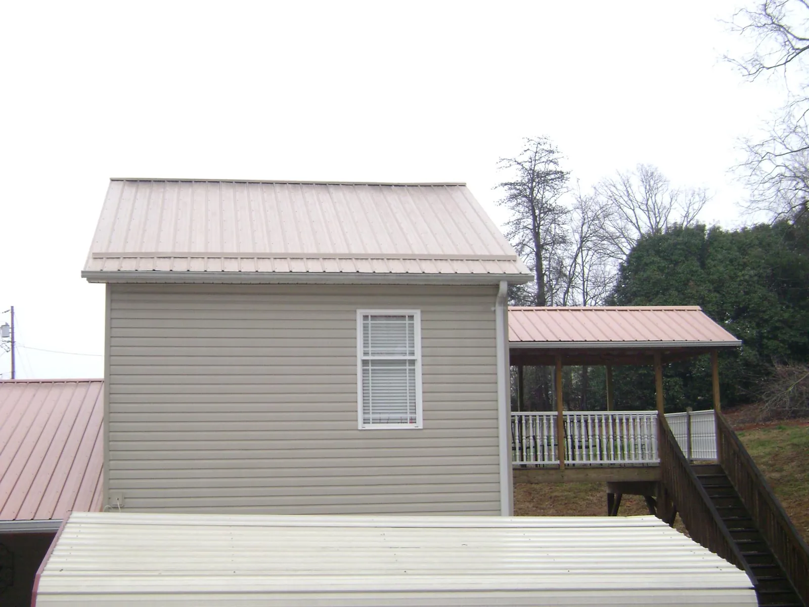 Tan metal roofs on a two story addition and attached porch, from a Roof Replacement job in Enigma